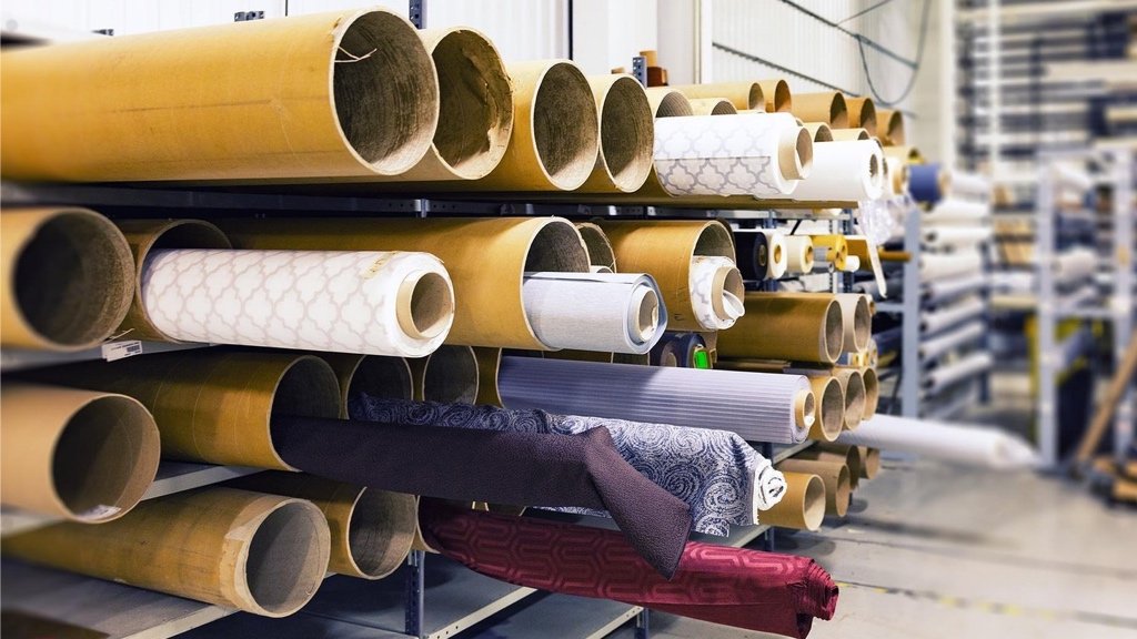 Buscando telas sostenibles y eligiendo el método de producción adecuado Diseñador de moda revisando rollos de tela y opciones de fabricación